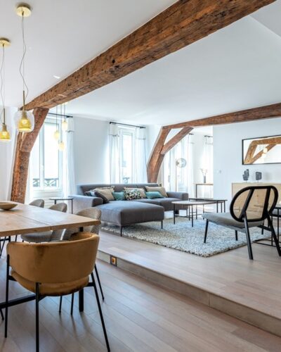 Salon élégant et moderne d’un pied-à-terre au centre de Paris, avec poutres apparentes et une ambiance lumineuse et raffinée.