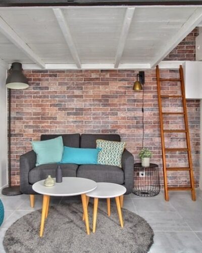 Salon avec murs en briques apparentes, canapé moderne, échelle menant à une mezzanine, situé dans un studio à Montmartre, Paris 18e, proposé par un chasseur immobilier expert à Paris.