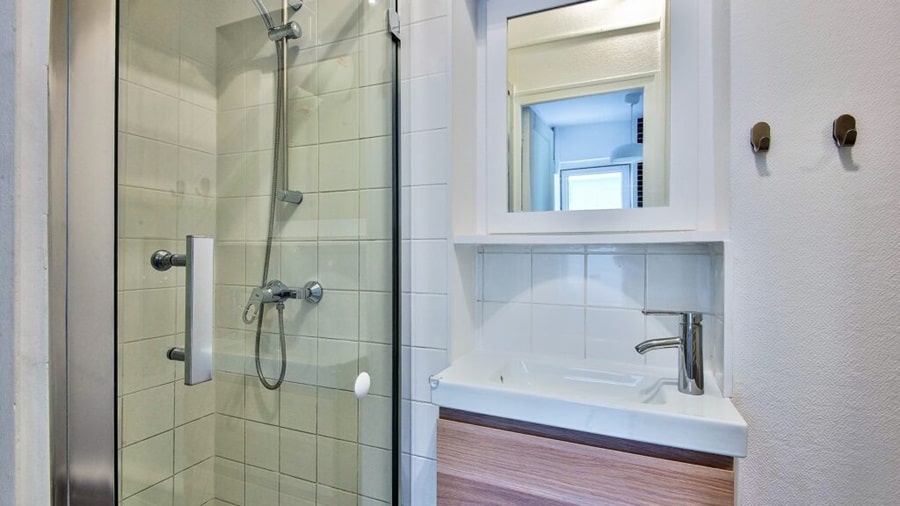 Salle de bain compacte et moderne avec une cabine de douche en verre, un meuble vasque en bois et un miroir intégré, idéale pour un appartement rénové à Asnières-sur-Seine.