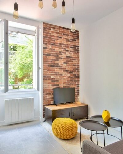 Salon lumineux et moderne avec mur en briques apparentes dans un appartement à Asnières, idéal pour un investissement locatif proche de la gare