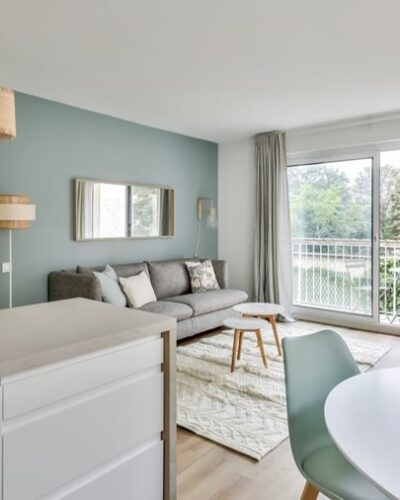 Salon moderne avec cuisine ouverte, parquet clair, et vue dégagée sur un espace vert, dans un appartement situé dans le 5e arrondissement de Paris, proche du Jardin du Luxembourg, proposé par un chasseur immobilier à Paris.