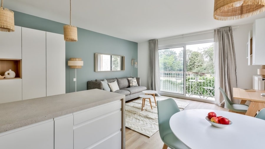 Salon moderne avec cuisine ouverte, parquet clair, et vue dégagée sur un espace vert, dans un appartement situé dans le 5e arrondissement de Paris, proche du Jardin du Luxembourg, proposé par un chasseur immobilier à Paris.