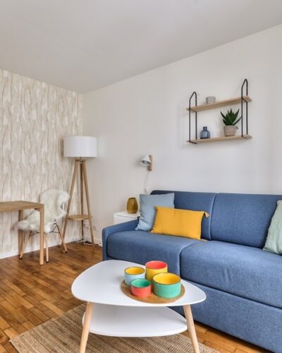 Studio lumineux avec décoration moderne, parquet en bois, canapé convertible bleu et coin repas, situé dans le 15e arrondissement de Paris, à proximité du métro Convention, proposé par un chasseur d'appartement à Paris.