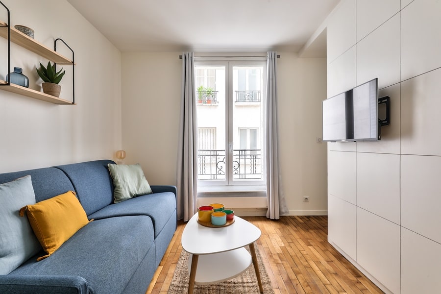 Salon lumineux d'un studio rénové à Paris avec parquet en bois, canapé bleu et décoration moderne - investissement locatif clé en main
