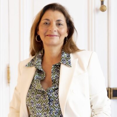 Portrait d'une chasseuse immobilière de l'équipe Early Birds, souriante et professionnelle, portant une veste blanche et une chemise à motifs