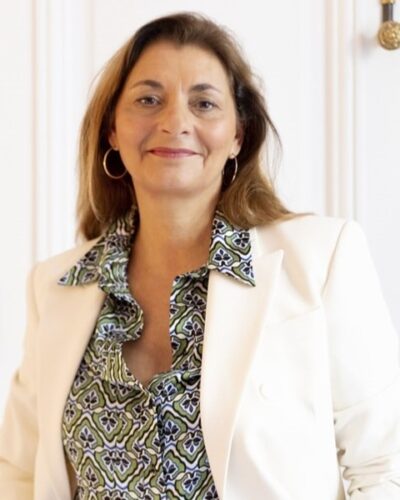 Portrait d'une chasseuse immobilière de l'équipe Early Birds, souriante et professionnelle, portant une veste blanche et une chemise à motifs