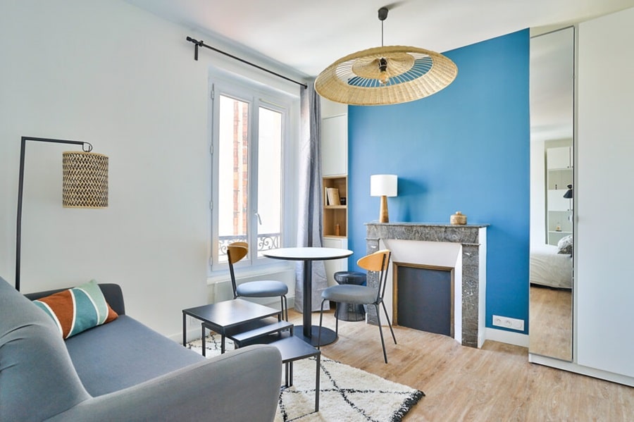 Salon lumineux avec mur bleu accent, mobilier moderne, cheminée décorative et coin repas, dans un studio situé à Asnières-sur-Seine, à proximité de la gare.