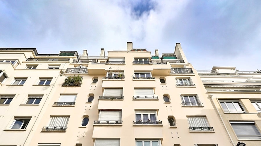 Vue de la façade d'un immeuble haussmannien rénové, lumineux et élégant, avec des balcons et des détails architecturaux uniques à Paris 16e.
