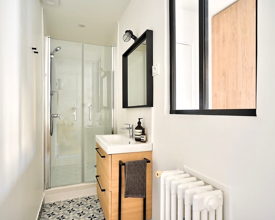 Salle de bain moderne et lumineuse avec une douche à l'italienne, un meuble lavabo en bois clair, et une verrière noire élégante pour un style industriel chic.
