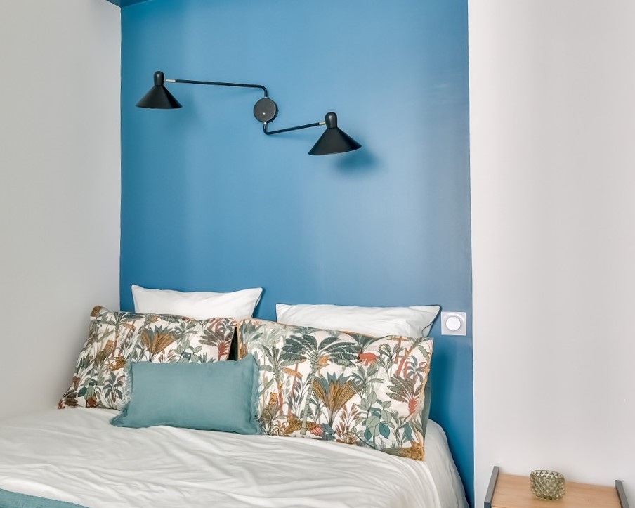 Chambre moderne et lumineuse avec un mur bleu, des luminaires design, et des oreillers à motifs