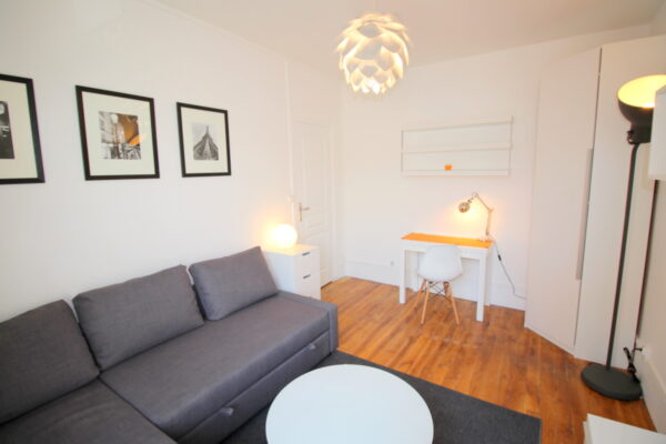 Salon spacieux et lumineux avec un canapé gris, un bureau design et une décoration minimaliste dans un appartement au centre-ville de Clichy (92)