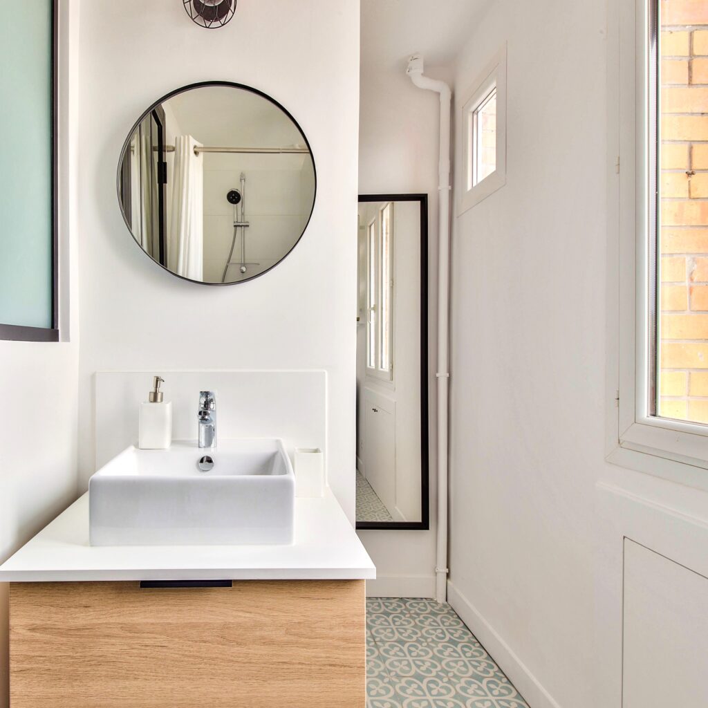 Salle de bain élégante avec vasque design, miroir rond et lumière naturelle, dans un 2 pièces à Asnières, proche du métro, proposé par Early Birds chasseurs immobiliers.
