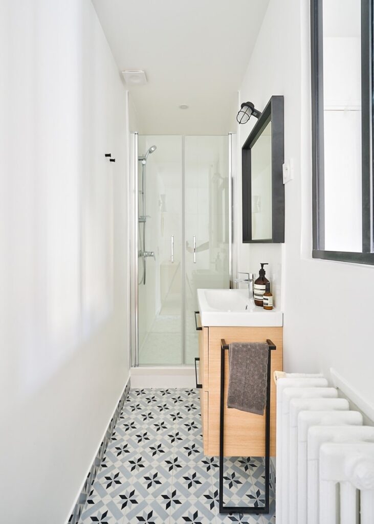 Salle de bain moderne avec douche à l’italienne, meuble vasque en bois clair et carrelage graphique noir et blanc dans un appartement rénové à Paris 16e.