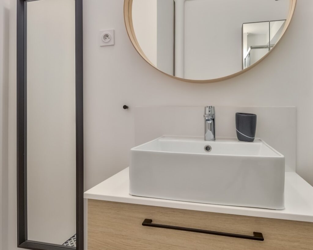 Salle de bain élégante avec vasque blanche, miroir rond en bois et éclairage moderne dans un appartement à Paris 16, Auteuil.