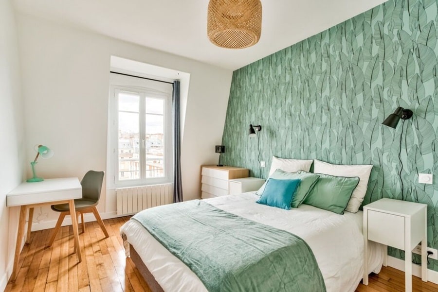 Chambre moderne et lumineuse avec un lit double, un bureau, et un mur texturé vert dans un deux-pièces au dernier étage aux Batignolles, Paris 17e, idéal pour un achat ou un investissement locatif.