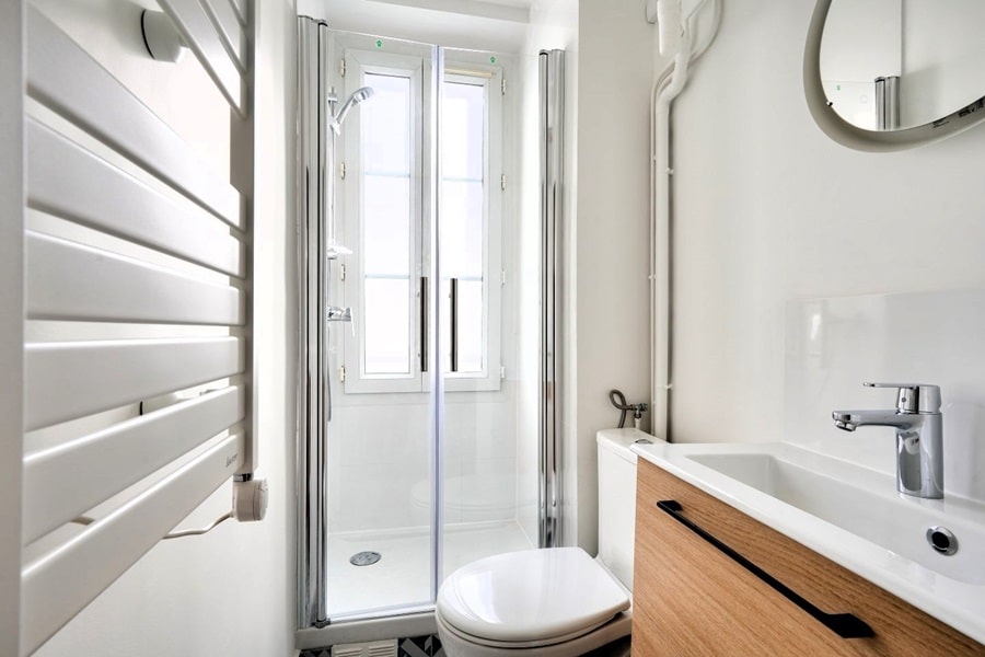 Salle de bain rénovée avec douche à l’italienne, meuble vasque contemporain et fenêtre lumineuse dans un studio du 14e arrondissement de Paris.