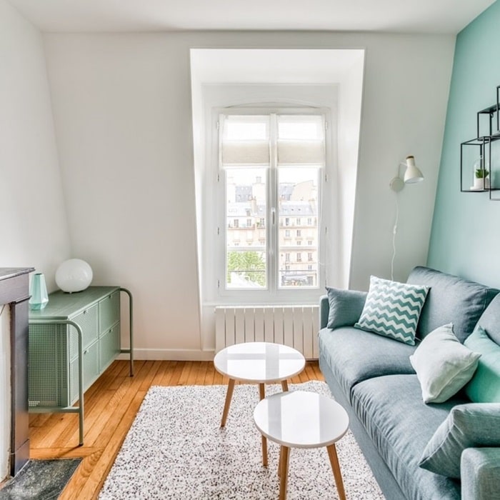 Salon lumineux avec parquet, canapé bleu, et décoration moderne, dans un deux-pièces au dernier étage aux Batignolles, Paris 17e, offrant une vue dégagée sur les toits parisiens.