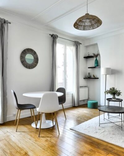 Salon lumineux avec parquet en bois, table à manger ronde blanche, canapé d'angle gris, et décoration moderne, dans un appartement du quartier Commerce à Paris 15e.