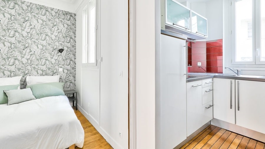 Une chambre lumineuse avec un papier peint tropical et une cuisine équipée moderne avec une crédence rouge, dans un appartement à Paris.