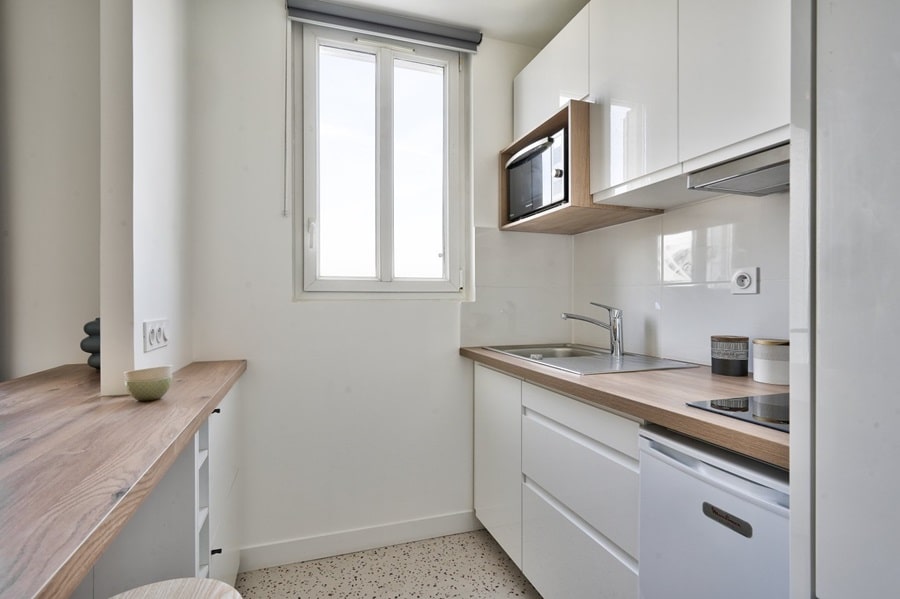 Cuisine moderne et compacte dans un appartement rénové à Bois-Colombes, avec des finitions blanches et un plan de travail en bois.