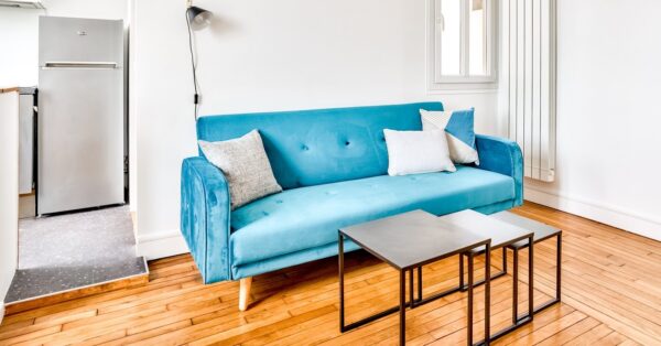 Petit salon chaleureux avec parquet, canapé bleu moderne et tables gigognes, idéal pour un investissement locatif, repéré par Early Birds, chasseurs immobiliers à Paris et ses environs, à Colombes.