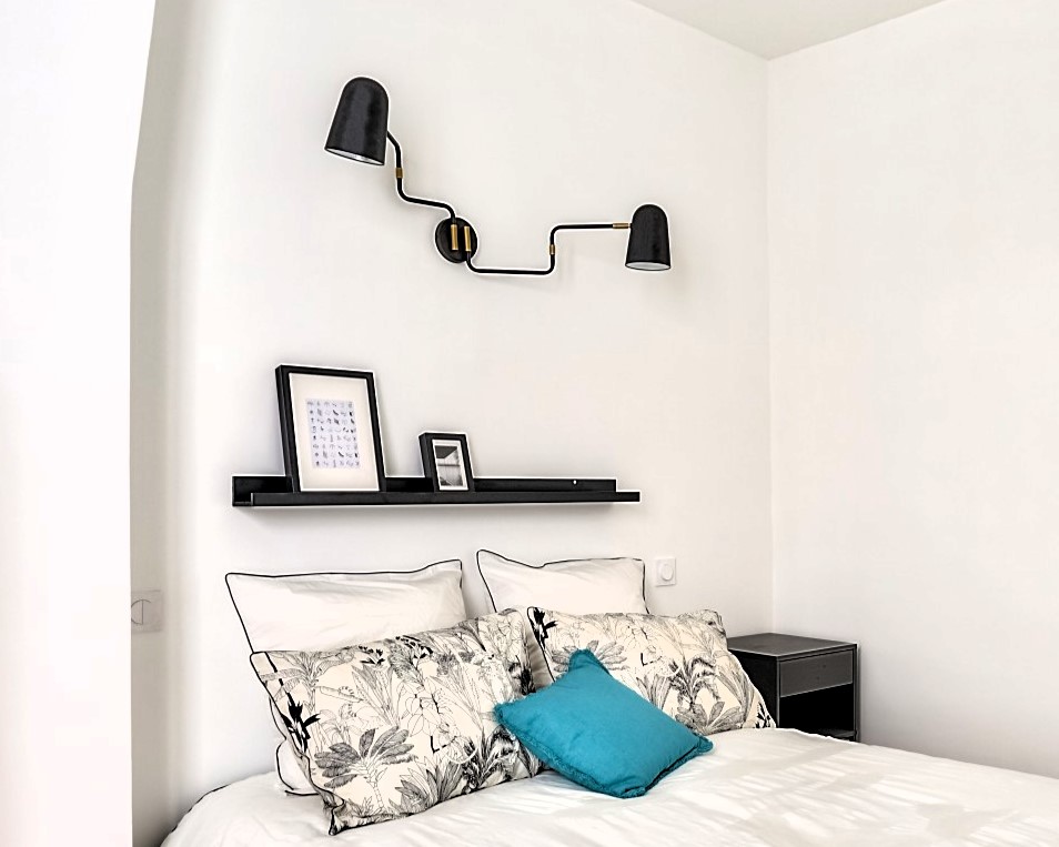 Chambre élégante et minimaliste avec des coussins floraux et une applique murale design, dans un appartement rénové à Paris 16e, Auteuil.