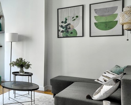 Coin salon avec canapé gris, tables d'appoint modernes et décoration murale verte.