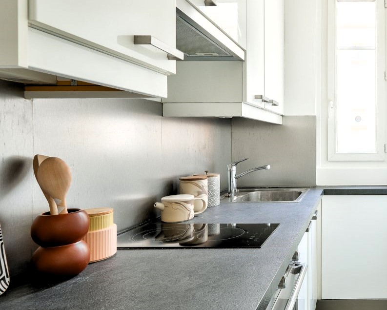 Cuisine moderne équipée avec plan de travail en pierre, éléments en inox, et vue sur l'extérieur.
