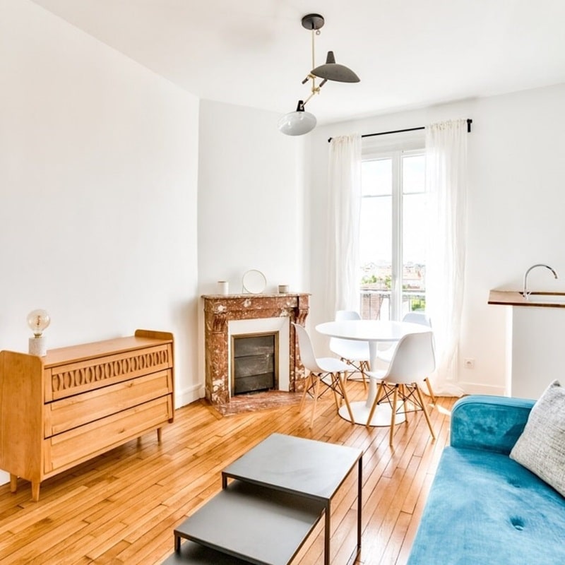 Salon lumineux avec parquet en bois, cheminée en marbre, mobilier vintage et espace repas, idéal pour un investissement locatif, sélectionné par Early Birds, chasseurs immobiliers à Paris et ses environs, à Colombes.