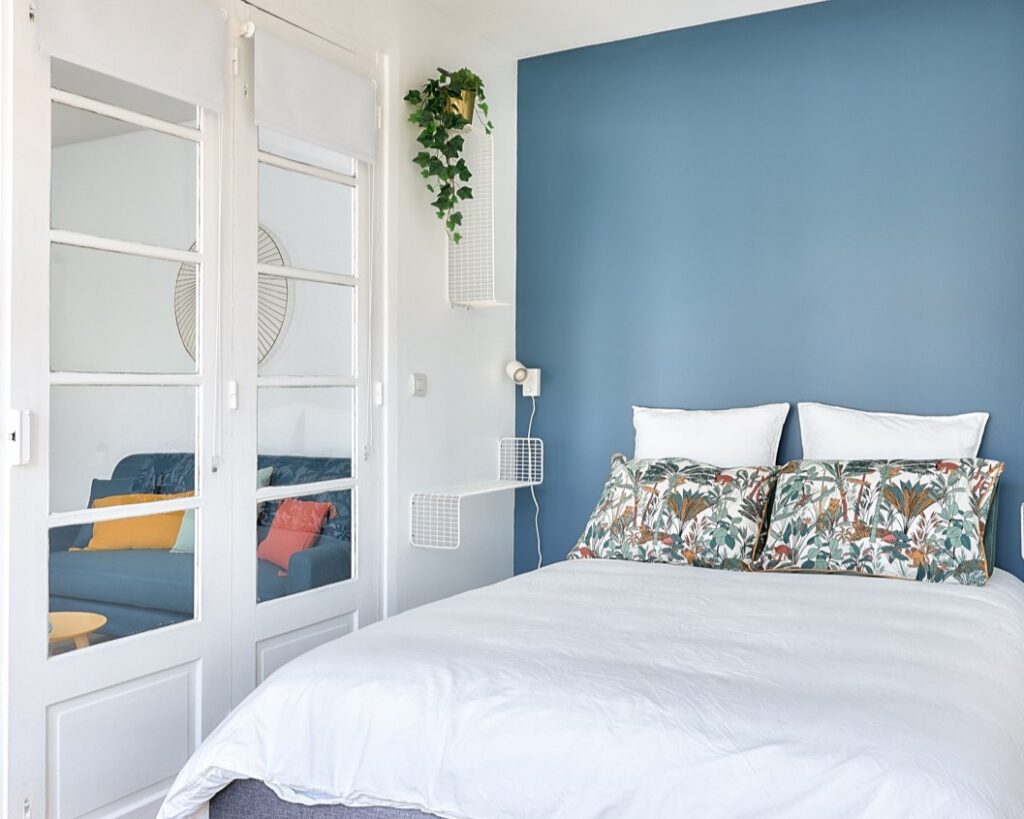 Chambre élégante avec un mur bleu, literie confortable et verrière donnant sur le salon, située Rue Sébastopol à La Garenne-Colombes, choisie par Early Birds, chasseurs immobiliers à Paris et ses environs.