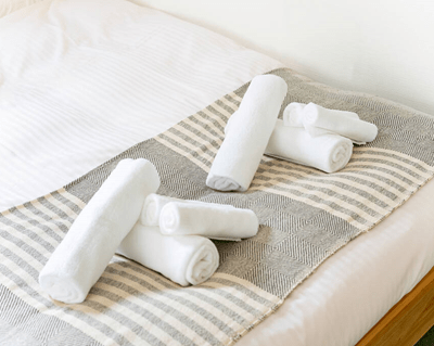 Serviettes blanches soigneusement disposées sur un lit avec une couverture à rayures, illustrant l'importance de l'accueil et du confort dans les logements adaptés à la location courte durée, type Airbnb, à Paris