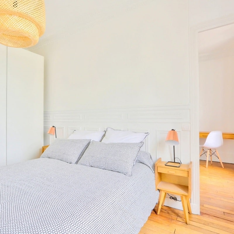 Chambre lumineuse avec mobilier en bois clair, lampes modernes, et parquet ancien, située près de la mairie d’Asnières-sur-Seine, idéale pour un investissement locatif.