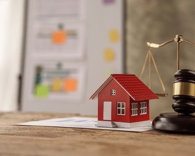 Représentation symbolique de la conformité juridique avec une maquette de maison rouge, une balance de justice et un marteau de juge, soulignant l'importance des règles pour les locations courte durée à Paris, type Airbnb