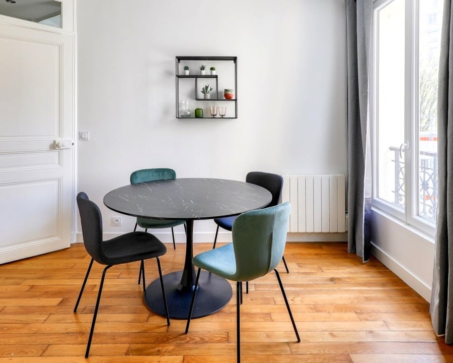Salle à manger lumineuse avec une table ronde en marbre noir et des chaises modernes, dans un 2 pièces situé à Paris 12e arrondissement.