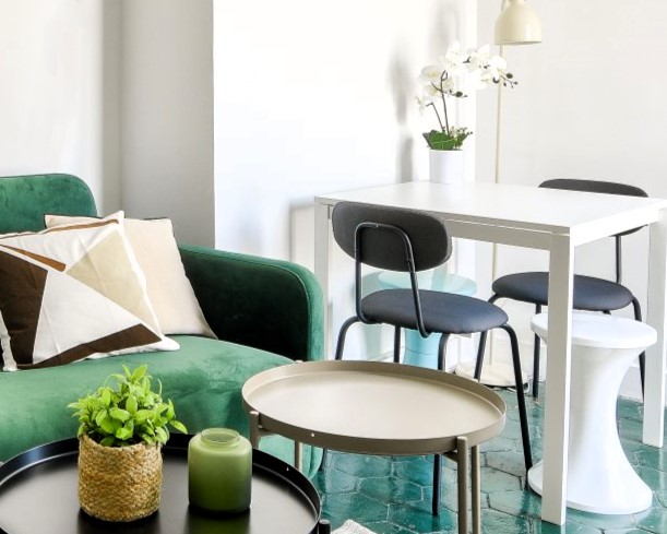 Salon lumineux avec un canapé vert, une table basse ronde, une table à manger blanche et des chaises noires, dans un appartement de la rue Mazarine, Paris 6e.