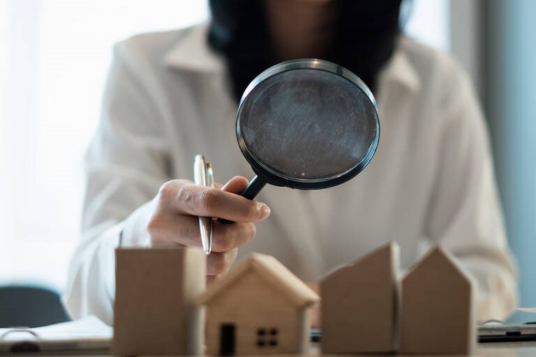 Une femme tenant une loupe et examinant des modèles de maisons, symbolisant l’expertise d’un chasseur immobilier dans l’évaluation et la recherche de biens à Paris et ses environs