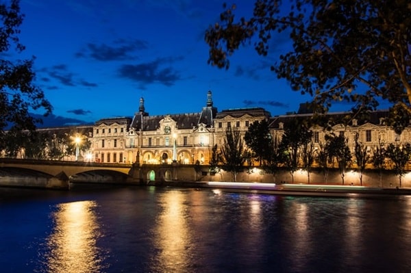 Le musée du Louvre illuminé la nuit, reflété sur la Seine, une vue emblématique du 1er arrondissement de Paris, parfait pour un projet immobilier prestigieux avec Early Birds Paris.