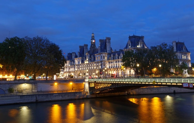Vue nocturne de l’Hôtel de Ville de Paris et du pont d’Arcole, un repère historique près du 3ᵉ arrondissement, prisé pour ses biens immobiliers de caractère.