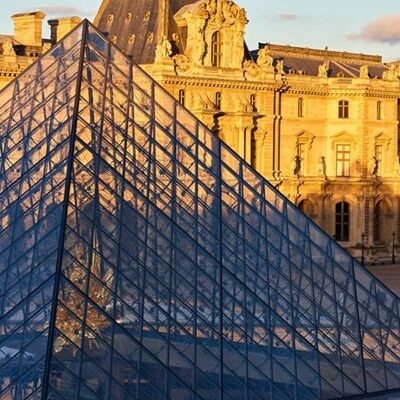 Vue sur la pyramide de verre et la façade du musée du Louvre au coucher de soleil, dans le 1er arrondissement de Paris, idéal pour une recherche immobilière prestigieuse avec Early Birds Paris.