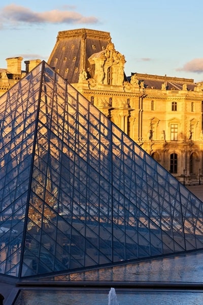 Vue sur la pyramide de verre et la façade du musée du Louvre au coucher de soleil, dans le 1er arrondissement de Paris, idéal pour une recherche immobilière prestigieuse avec Early Birds Paris.