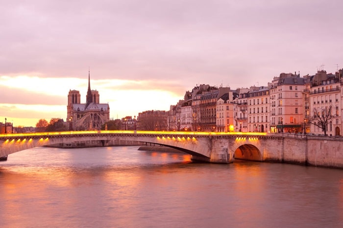 Pont illuminé et vue sur Notre-Dame de Paris au crépuscule, un paysage emblématique du 4ᵉ arrondissement, idéal pour un projet immobilier d'exception.