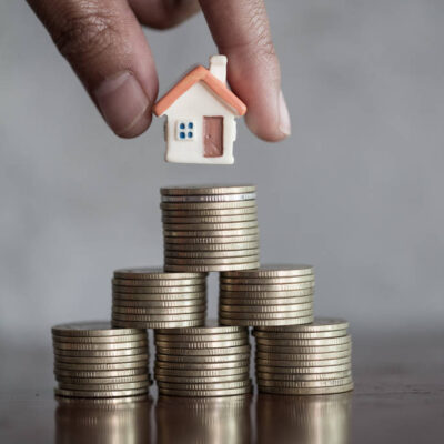 Représentation d'une maison miniature posée sur des piles de pièces de monnaie, illustrant le rendement locatif et l'investissement immobilier à Paris