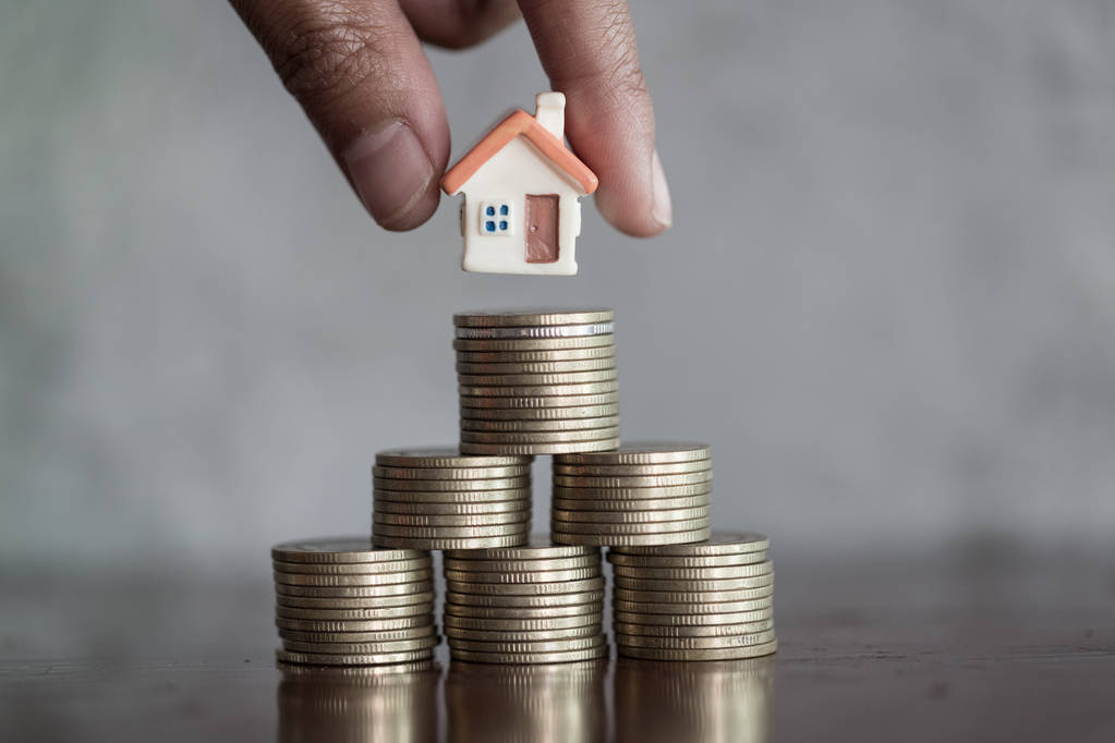 Représentation d'une maison miniature posée sur des piles de pièces de monnaie, illustrant le rendement locatif et l'investissement immobilier à Paris