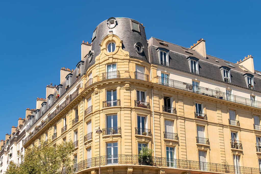 Immeuble haussmannien parisien avec pierres de taille, balcons filants et toit en zinc, photographié sous un ciel bleu dans un quartier résidentiel calme.