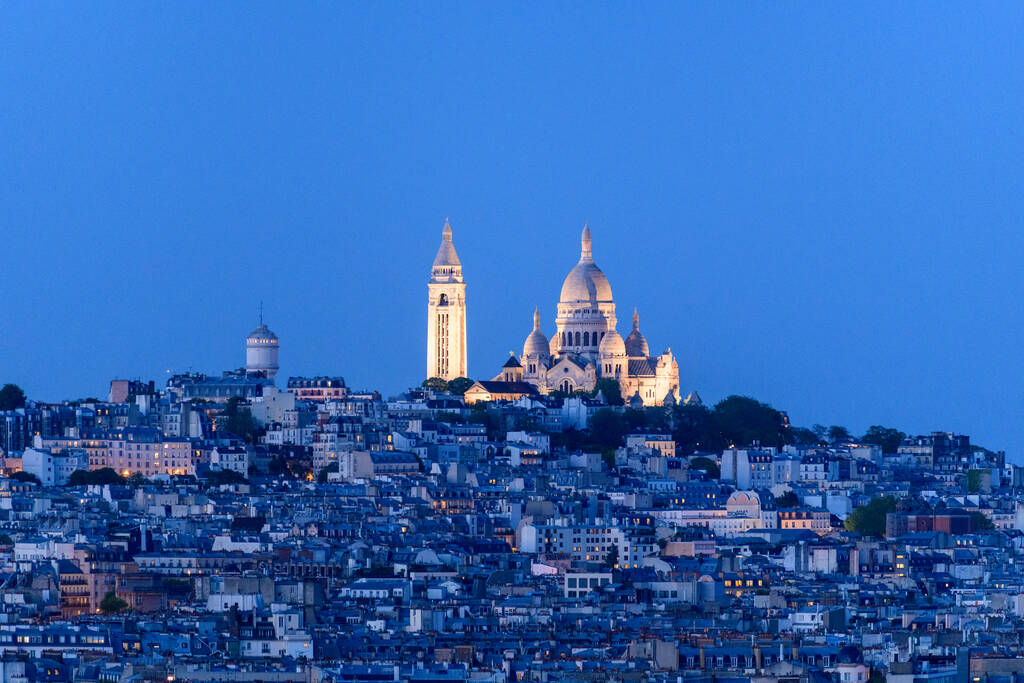 Panorama de Montmartre au bleu du soir avec la basilique du Sacré-Cœur illuminée dominant les toits parisiens.