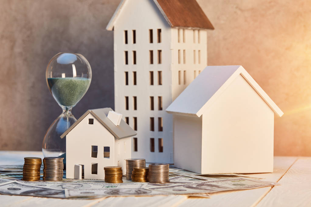 Représentation du financement immobilier avec maisons miniatures, argent et notion de délai avant un achat immobilier