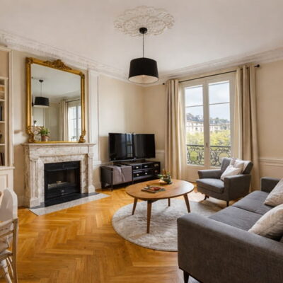 Séjour lumineux d’un appartement trois pièces à Paris avec parquet, cheminée et fenêtres sur cour