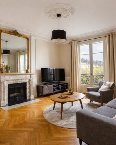 Séjour lumineux d’un appartement trois pièces à Paris avec parquet, cheminée et fenêtres sur cour