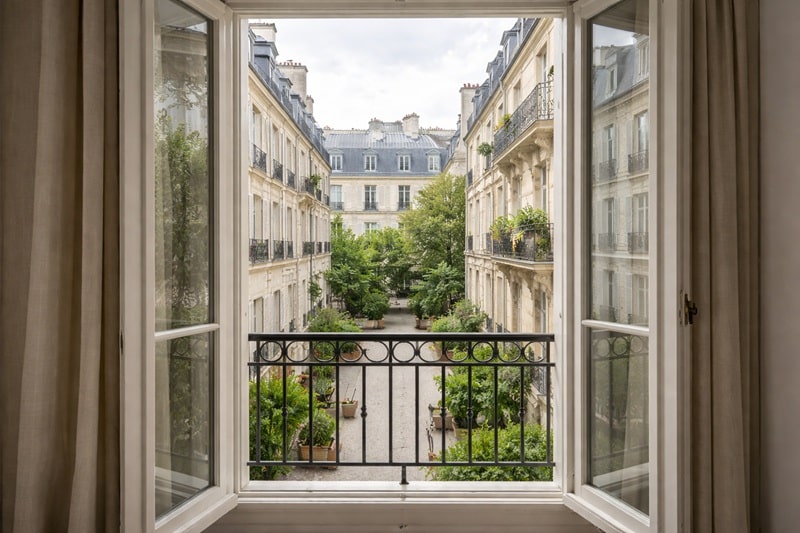 Vue dégagée sur une cour intérieure parisienne depuis une fenêtre, apportant calme, verdure et luminosité dans un appartement traversant.