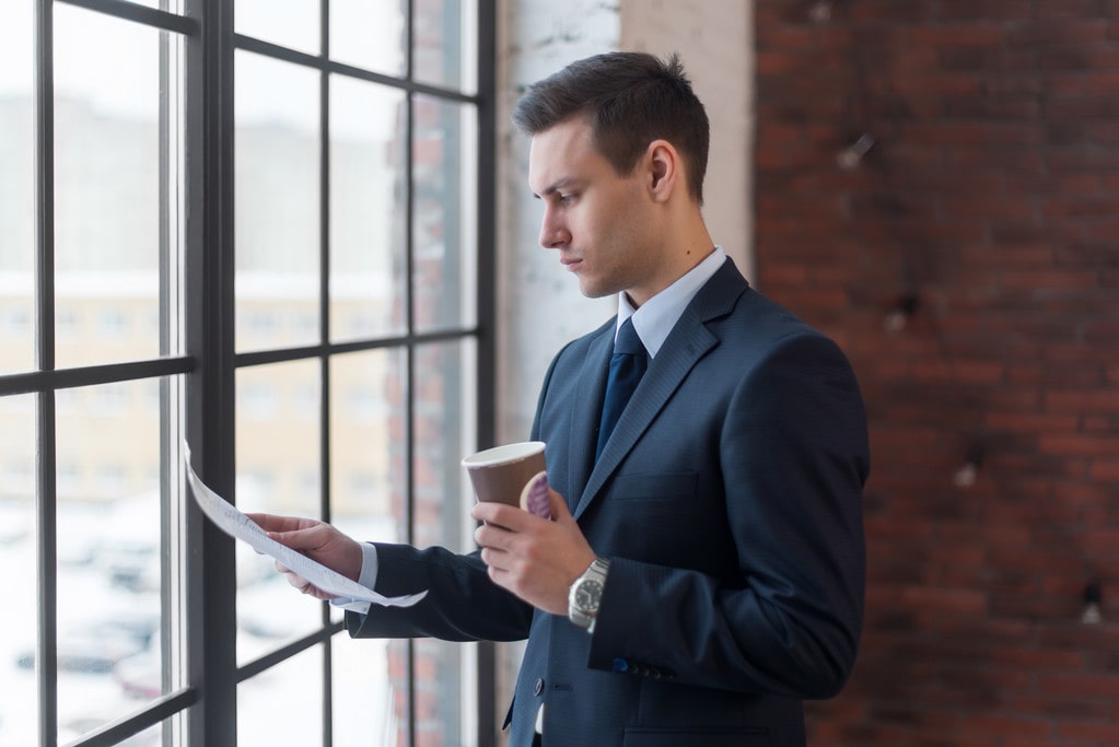 Acheteur immobilier professionnel examinant des documents de compromis de vente devant une fenêtre